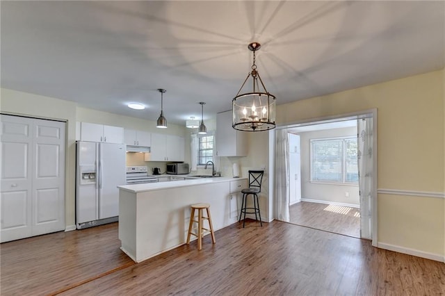 kitchen with light hardwood / wood-style flooring, kitchen peninsula, pendant lighting, white appliances, and white cabinets