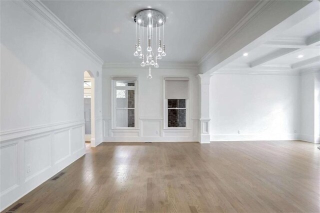 unfurnished living room with an inviting chandelier, beam ceiling, decorative columns, wood-type flooring, and ornamental molding