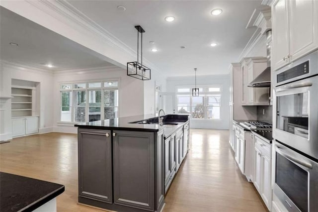 kitchen with appliances with stainless steel finishes, white cabinetry, a center island with sink, decorative light fixtures, and light wood-type flooring