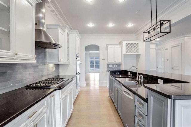 kitchen featuring wall chimney exhaust hood, decorative light fixtures, ornamental molding, stainless steel appliances, and white cabinets