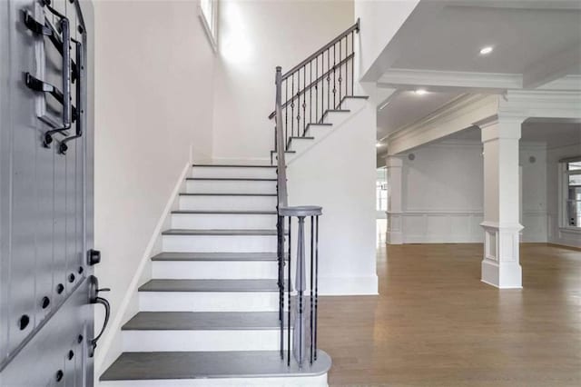 stairs with decorative columns, wood-type flooring, and crown molding