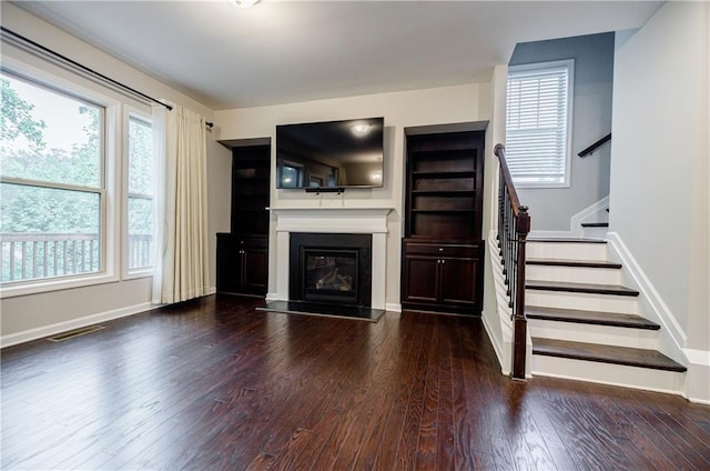 unfurnished living room featuring stairs, wood finished floors, plenty of natural light, and a glass covered fireplace
