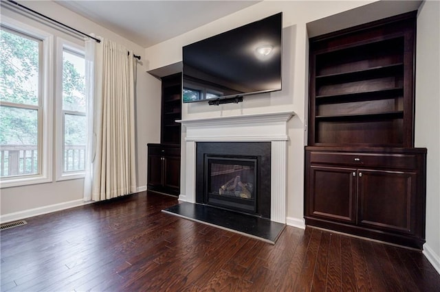 unfurnished living room featuring dark wood-type flooring, a glass covered fireplace, and baseboards