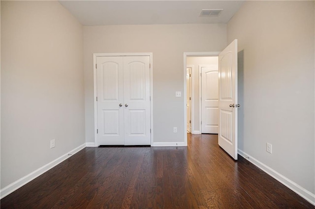 unfurnished bedroom with dark wood finished floors, baseboards, and a closet