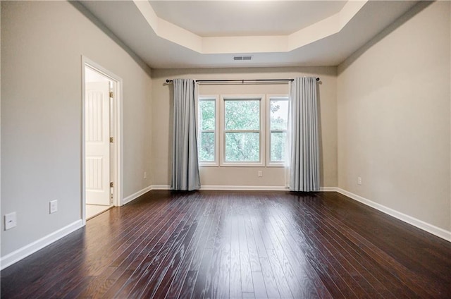 empty room with a raised ceiling, dark wood-type flooring, and baseboards