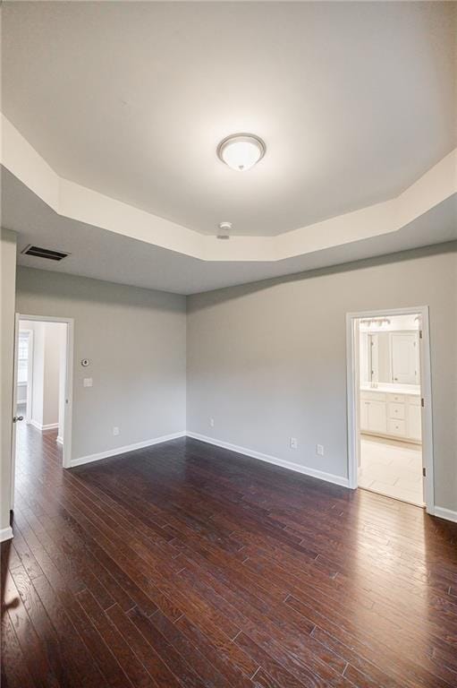 unfurnished room featuring dark wood finished floors, baseboards, and a raised ceiling