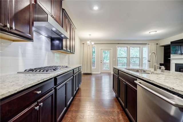 kitchen with stainless steel appliances, a sink, under cabinet range hood, a chandelier, and backsplash