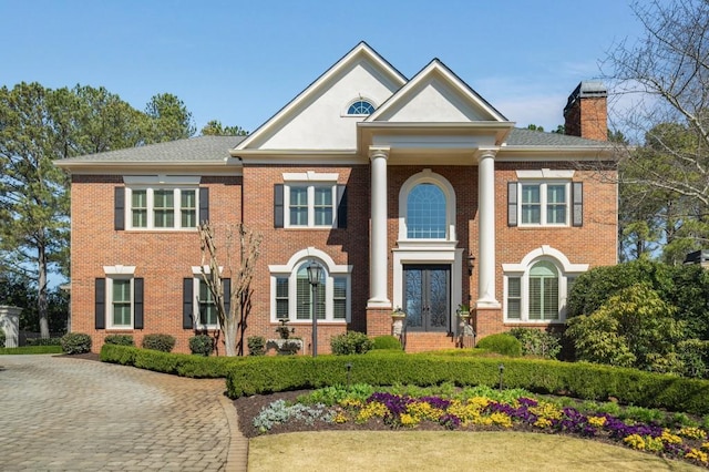 neoclassical / greek revival house with french doors, brick siding, and a chimney