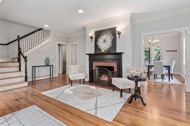 living room featuring a brick fireplace, ornamental molding, a notable chandelier, and light hardwood / wood-style flooring