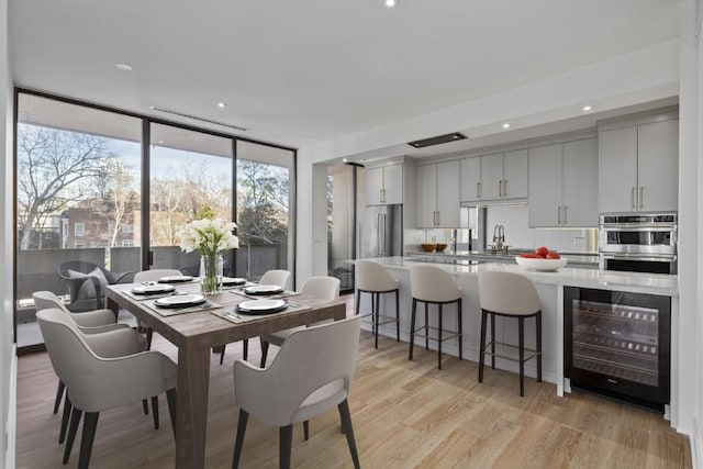 dining room featuring expansive windows, light wood-style flooring, wine cooler, and recessed lighting