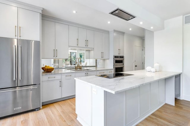 kitchen featuring light stone counters, recessed lighting, a sink, light wood-style floors, and appliances with stainless steel finishes