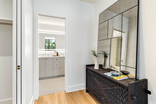 corridor with light wood-style flooring, baseboards, and a sink