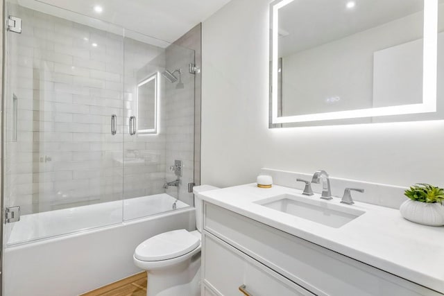 bathroom with vanity, toilet, wood finished floors, and shower / bath combination with glass door