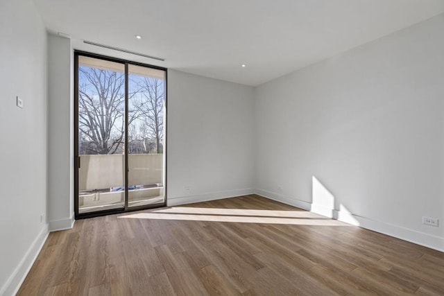 empty room with floor to ceiling windows, baseboards, and wood finished floors