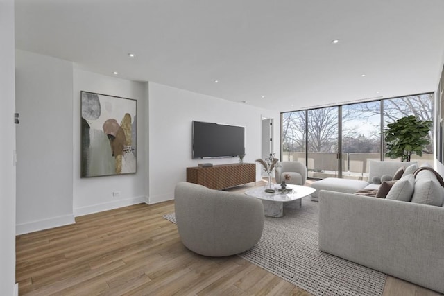 living room with light wood finished floors, a wall of windows, recessed lighting, and baseboards