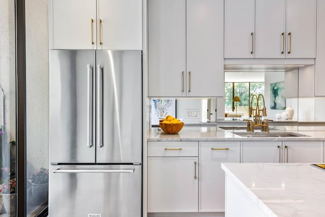 kitchen with light stone counters, a sink, high end refrigerator, white cabinetry, and tasteful backsplash