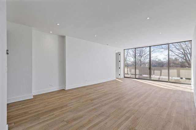 unfurnished room with recessed lighting, expansive windows, baseboards, and light wood finished floors