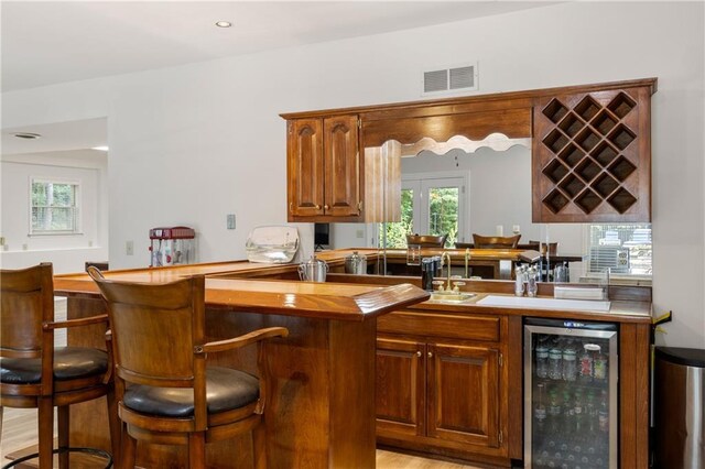 interior space with sink, light wood-type flooring, kitchen peninsula, and beverage cooler