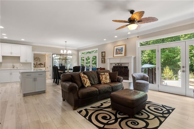 living room with light hardwood / wood-style flooring, a high end fireplace, sink, crown molding, and ceiling fan with notable chandelier