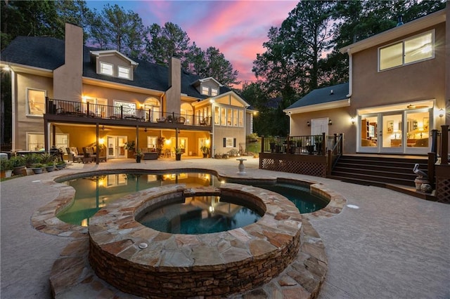 back of house at dusk with stucco siding, a wooden deck, a patio, and a balcony