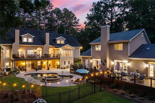 back house at dusk with a balcony, a lawn, and a patio area