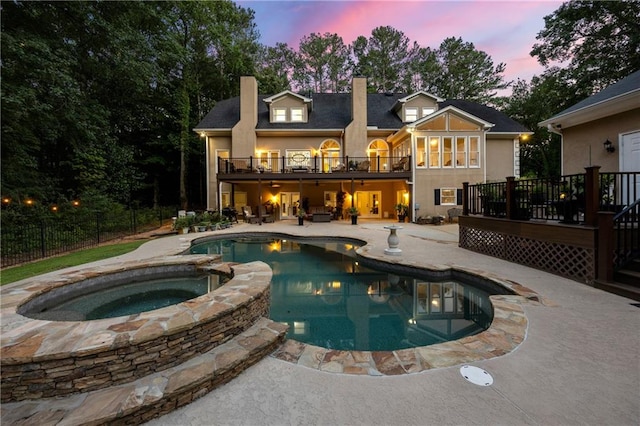 pool at dusk with an in ground hot tub and a patio