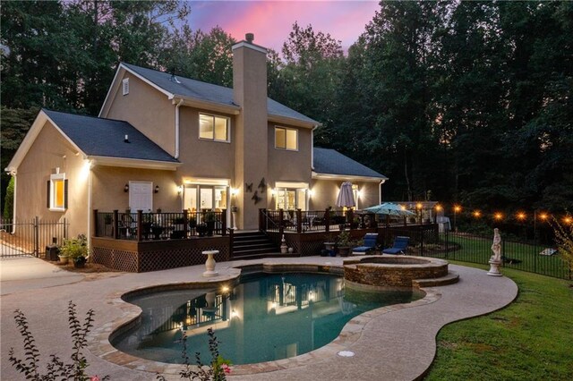 pool at dusk featuring an in ground hot tub, a deck, and a patio