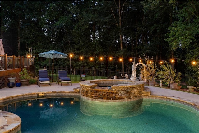 pool at night featuring an in ground hot tub