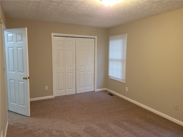 unfurnished bedroom featuring carpet flooring, baseboards, a closet, and a textured ceiling