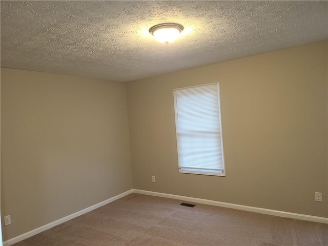 carpeted spare room featuring baseboards, visible vents, and a textured ceiling