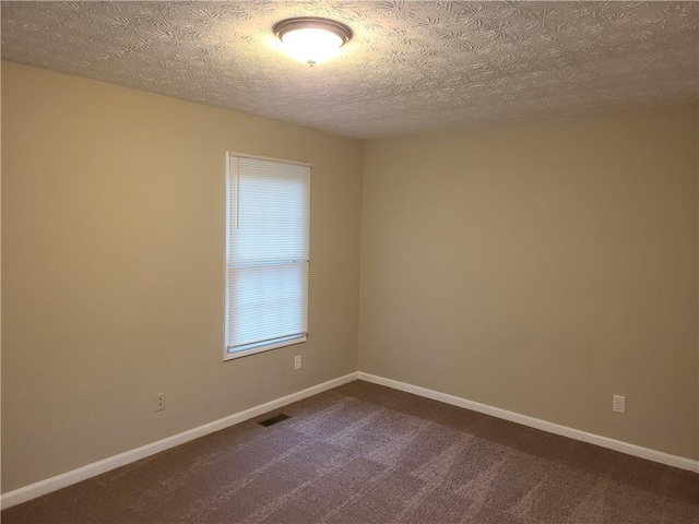 empty room featuring visible vents, baseboards, dark colored carpet, and a textured ceiling