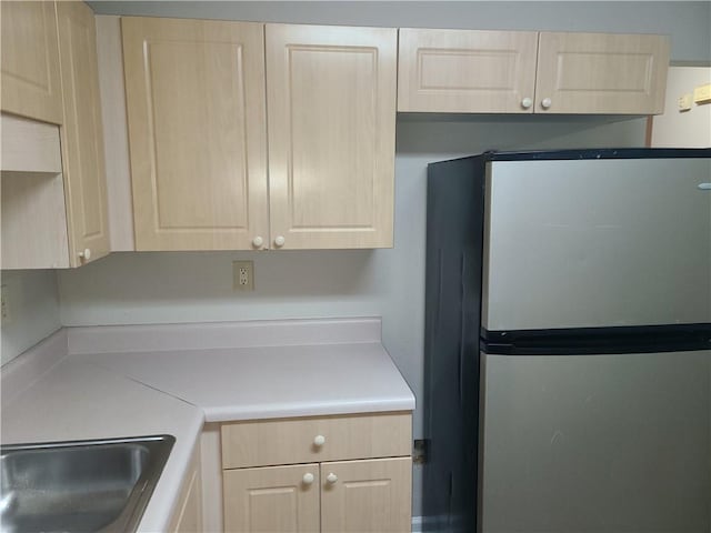 kitchen with light brown cabinets, light countertops, freestanding refrigerator, and a sink