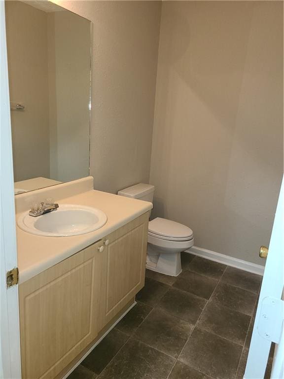 half bathroom featuring baseboards, toilet, and vanity