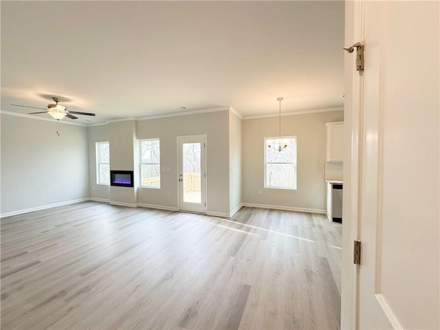 unfurnished living room with light wood-type flooring, ornamental molding, ceiling fan with notable chandelier, a glass covered fireplace, and baseboards