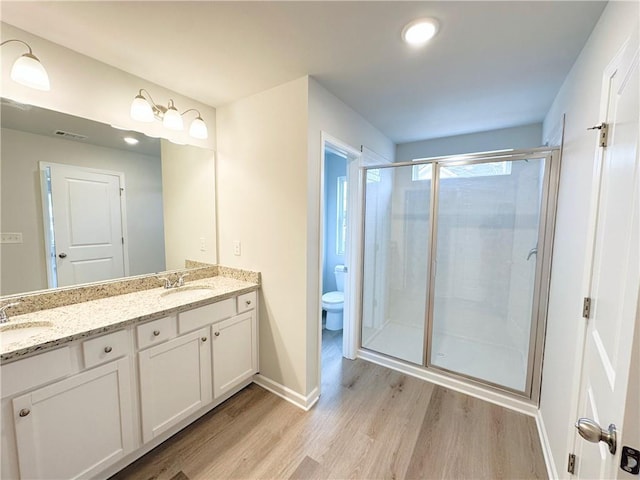 bathroom with visible vents, toilet, a stall shower, wood finished floors, and double vanity