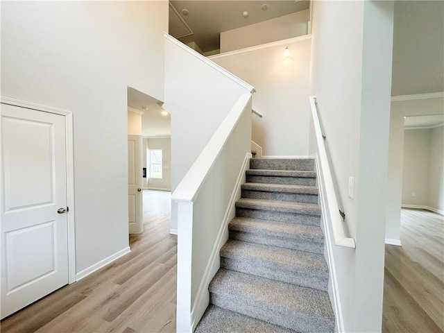 staircase with baseboards, wood finished floors, a towering ceiling, and ornamental molding