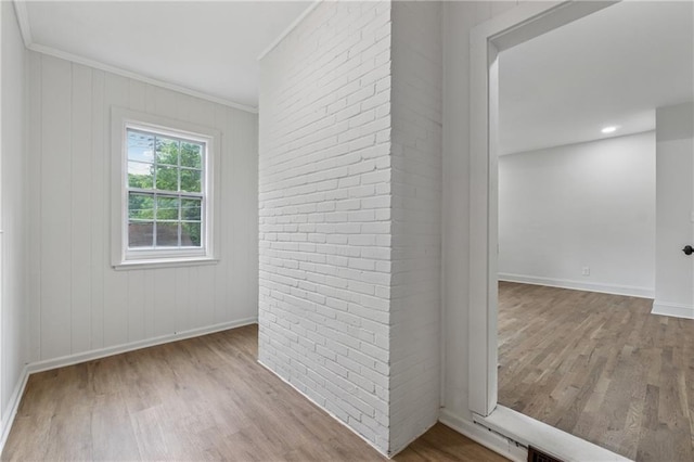 spare room with crown molding, brick wall, wood finished floors, and baseboards