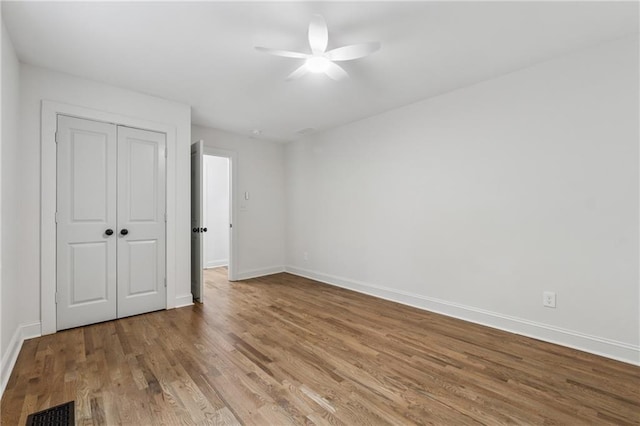 unfurnished bedroom with a closet, a ceiling fan, visible vents, baseboards, and wood finished floors