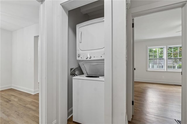 clothes washing area with stacked washing maching and dryer, wood finished floors, laundry area, and baseboards