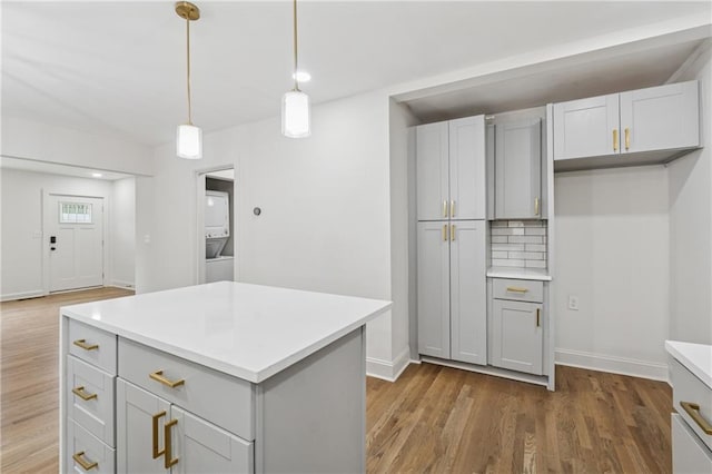kitchen with stacked washer / dryer, wood finished floors, decorative light fixtures, and light countertops