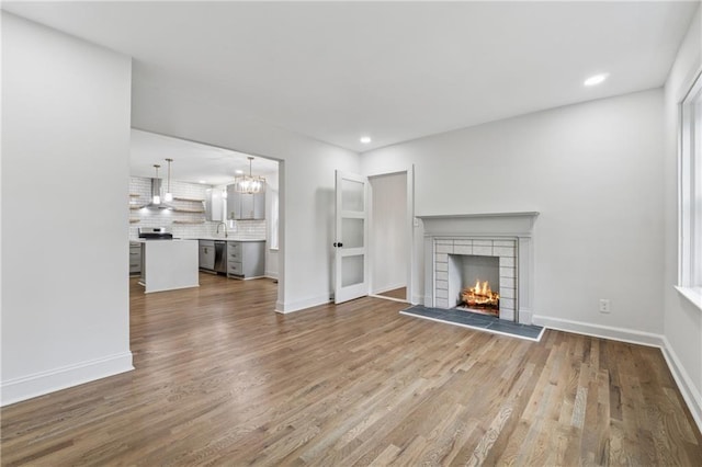 unfurnished living room with recessed lighting, dark wood-style flooring, a warm lit fireplace, a notable chandelier, and baseboards