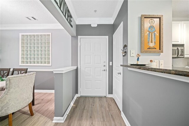 interior space with a textured ceiling, crown molding, and light hardwood / wood-style flooring