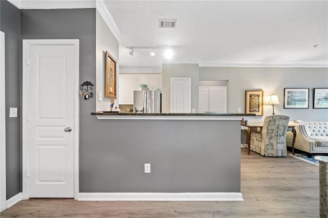 kitchen featuring light hardwood / wood-style flooring, dark stone countertops, ornamental molding, a textured ceiling, and stainless steel refrigerator