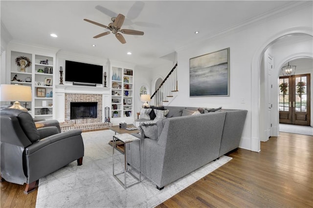 living room featuring ceiling fan, crown molding, wood-type flooring, and a brick fireplace