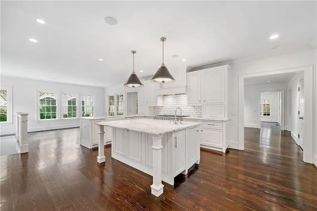 kitchen featuring white cabinetry, a healthy amount of sunlight, an island with sink, and pendant lighting