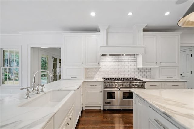 kitchen featuring sink, tasteful backsplash, light stone countertops, white cabinets, and range with two ovens