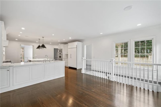 kitchen with dark hardwood / wood-style floors, decorative light fixtures, an island with sink, white cabinets, and built in appliances