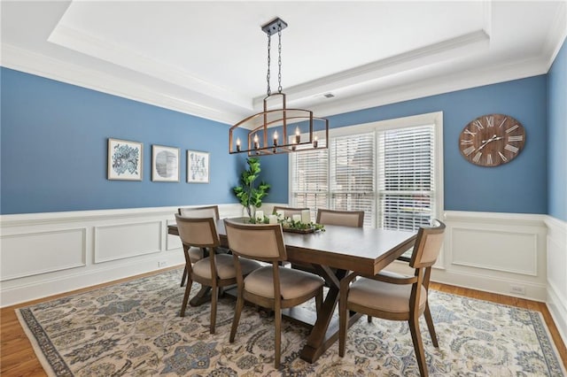 dining room with ornamental molding, wood-type flooring, an inviting chandelier, and a raised ceiling