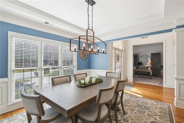 dining area with an inviting chandelier, light hardwood / wood-style flooring, ornamental molding, and a raised ceiling