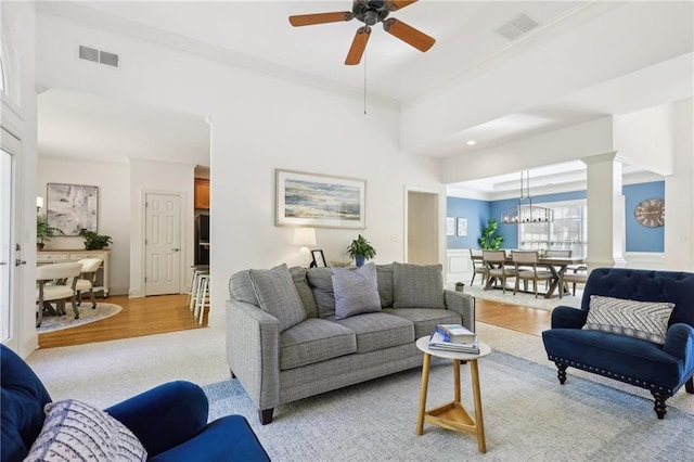 living room with decorative columns, ceiling fan with notable chandelier, and light hardwood / wood-style floors